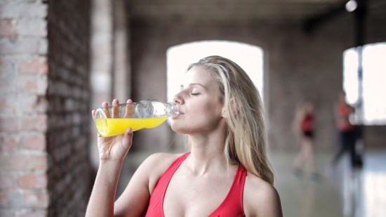 mujer en ropa de deporte con top rojo bebiendo zumo