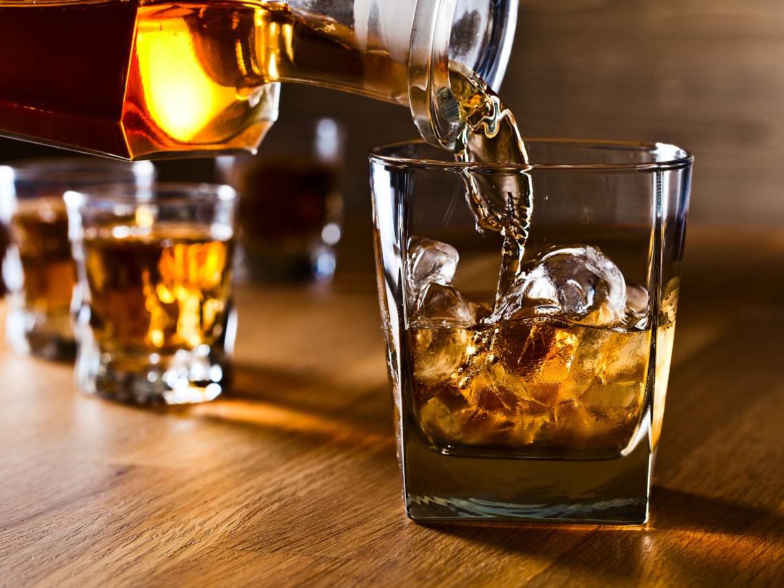 coctelera vertiendo whisky en vaso sobre mesa de madera