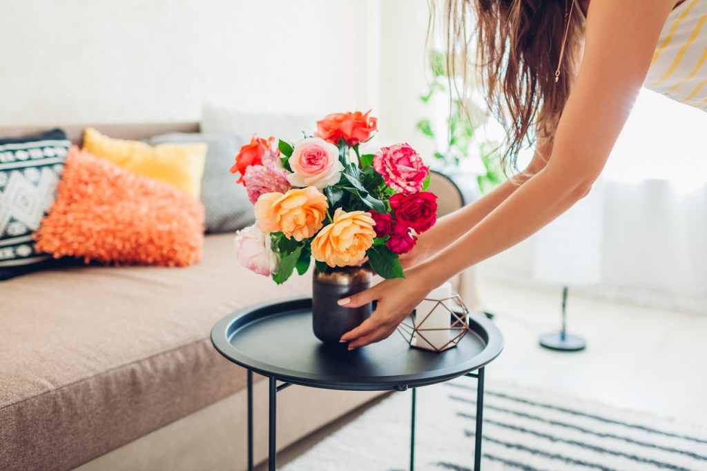 Mujer colocando un jarrón de flores en el salón - Imagen: iStock