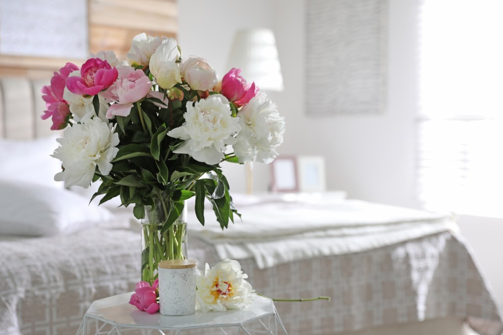 Ramo de peonías y vela perfumada en un dormitorio - Imagen: iStock